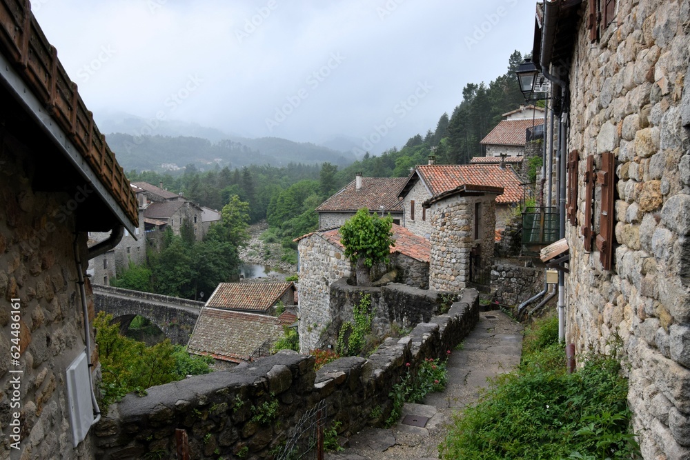 
Jaujac village in Ardeche, Massif Central, France, in the rain without people - dark, volcanic stone and flowing river under ancient stone bridge