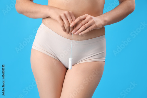 Young woman in menstrual panties with tampon on blue background, closeup