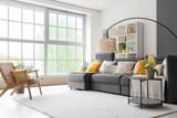 Interior of stylish living room with cozy grey sofa and wooden armchair near big window