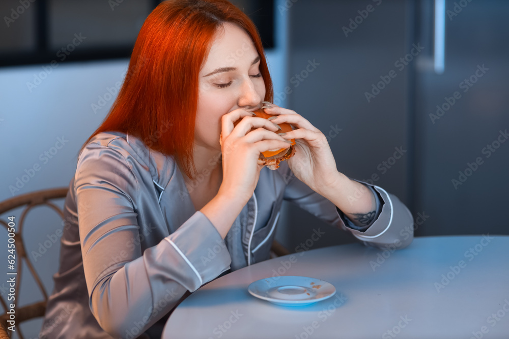 Young woman eating burger in kitchen at night Young woman eating burger in kitchen at night