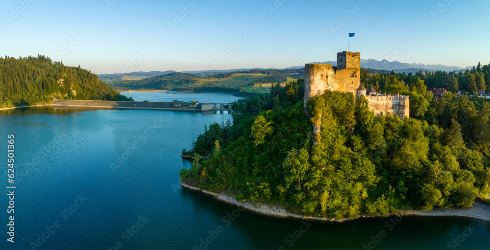 Poland. Medieval castle in Niedzica, 14th century (upper part) in sunset light. Artificial Czorsztyn lake on Dunajec river, damn and hydro power station. Tatra Mountains in the background. Aerial view