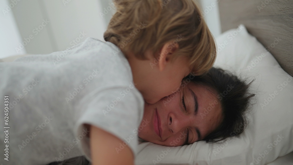 Little boy waking up mother in the morning jumping into mom and kissing Little boy waking up mother in the morning jumping into mom and kissing