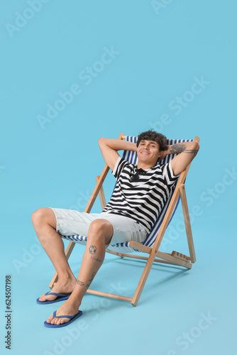 Young man sitting in deck chair on blue background