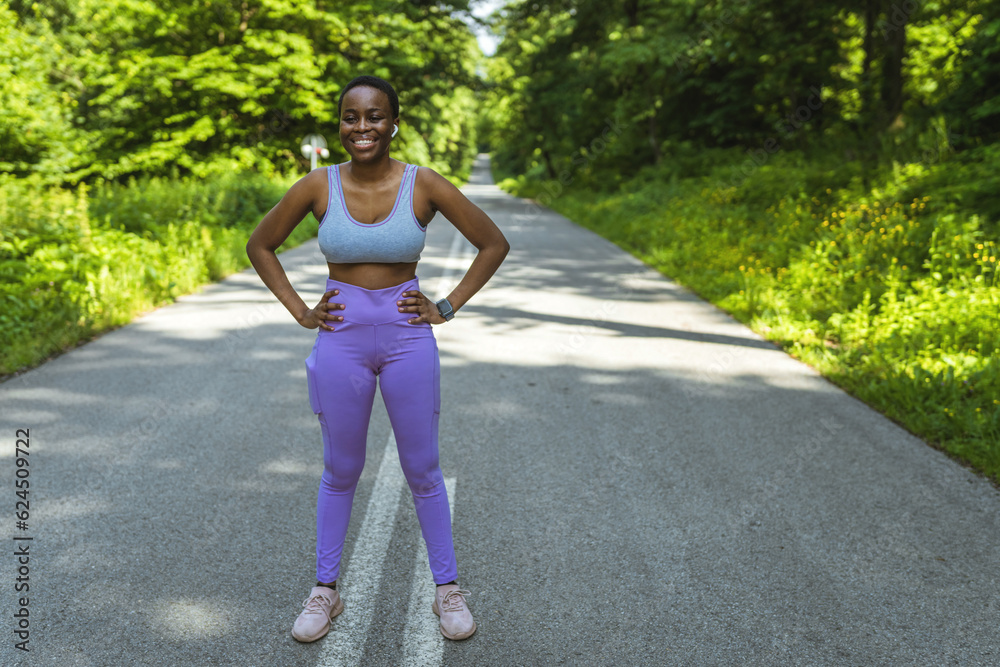 Woman athlete in running gear posing on empty road. Athlete standing on road early in the morning.