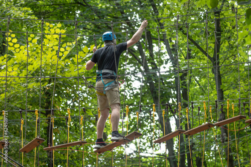 Vacationer in climbing gear in rope park in summer. Sports activity. Rope park. Alpinist equipment. A brave person. Fear of heights. Be on top. Summer leisure. Extreme sports.