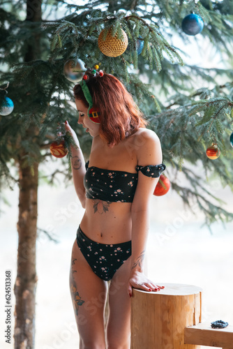 Beautiful girl in bikini with Christmas tree and snow-covered trees in winter