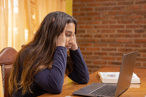 Frustrated latin girl, studying in front of a laptop.