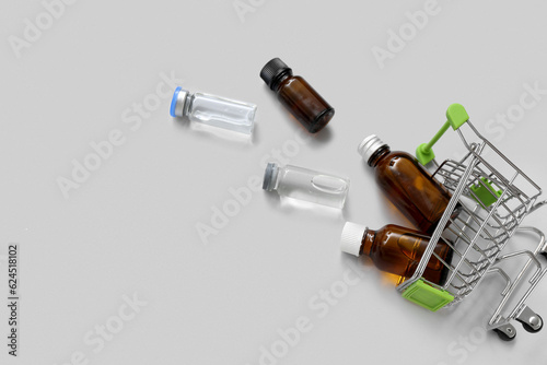 Mini shopping cart with different bottles of medicines on grey background