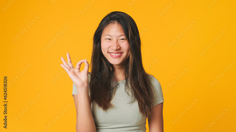 Girl in gray top looking at camera, smiling and showing okay ok zero fingers gesture isolated on yellow background in studio Girl in gray top looking at camera, smiling and showing okay ok zero fingers gesture isolated on yellow background in studio
