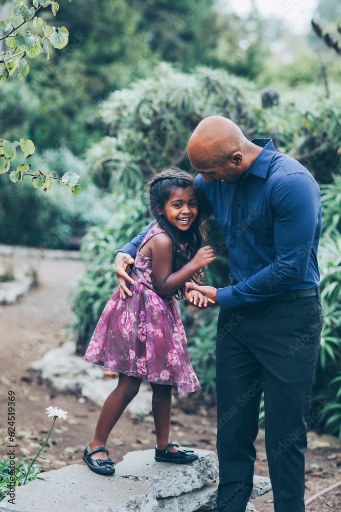 beautiful indian father playfully hugging his child daughter girl in the park with trees and greenery