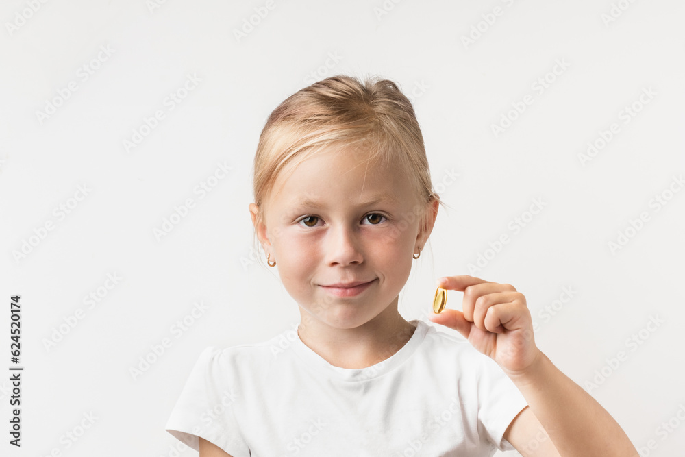 Portrait of happy cute little caucasian girl holding supplement capsule of Omega 3 on the white background. Multivitamin pill containing amino acid. Medicine with fish or krill oil source for kids Portrait of happy cute little caucasian girl holding supplement capsule of Omega 3 on the white background. Multivitamin pill containing amino acid. Medicine with fish or krill oil source for kids