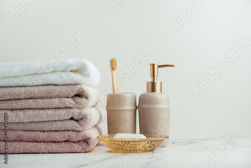 Vintage golden bath supplies with stack of clean soft towels next to soap and toothbrushes. White, pink and beige towels with bathroom accessories on the white background.