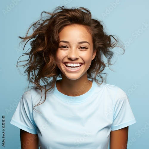 Portrait of a smiling young adult African woman with curly brown hair on a blue background. Happy young woman with a smile in a blue shirt with wavy hair. African American woman with shiny white teeth