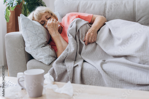 Senior woman being sick having flu lying on sofa. Sick older lady lying in bed with high fever.