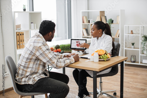 Canvas Print African american specialist in nutrition holding tablet with gastrointestinal tract on screen while counseling man at work