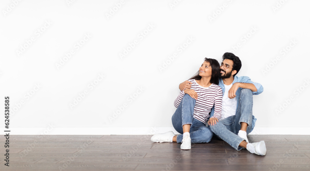 Beautiful happy hindu couple sitting on floor over white wall Beautiful happy hindu couple sitting on floor over white wall