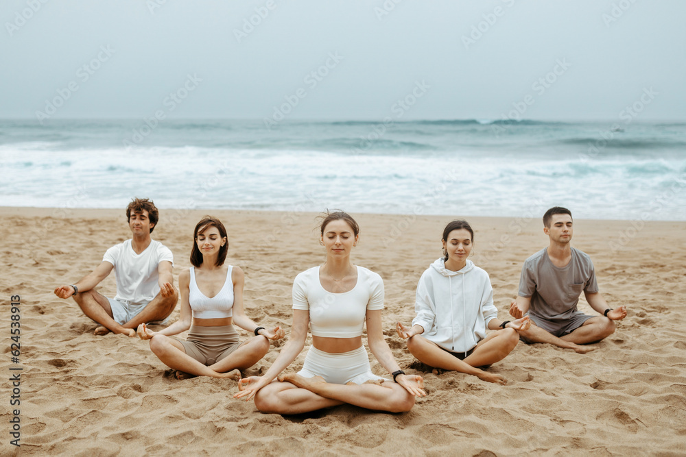 Meditation class outoors. Group of people practicing yoga on the beach, meditating with closed eyes in lotus position Meditation class outoors. Group of people practicing yoga on the beach, meditating with closed eyes in lotus position