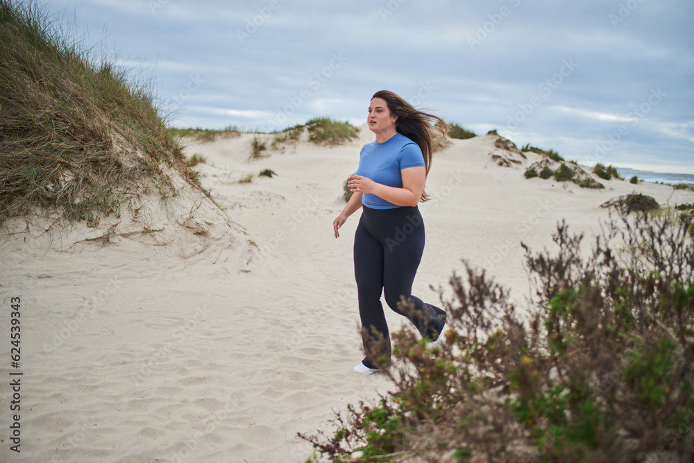 Young body positive sports woman running along the sandy sea shore