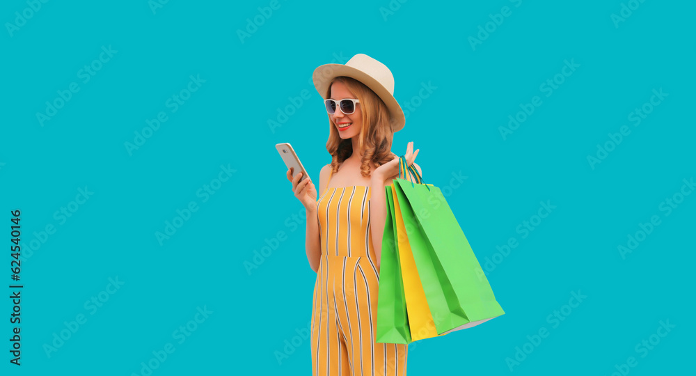 Beautiful happy young woman looking at phone with shopping bag wearing summer straw hat on blue background