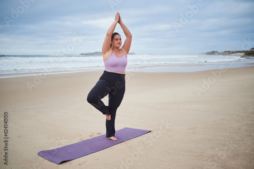 Calm fat woman practicing yoga in warrior pose at the cloudy ocean beach