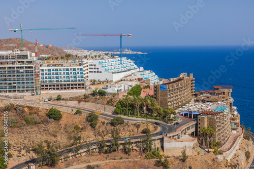 Beautiful top view of mountainous coast of Atlantic Ocean with moving cars on highway and hotels on mountain. Gran Canaria. Spain.