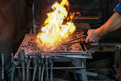 Foto Blacksmith holding a workpiece in the blazing coal fire on the forge to make the
