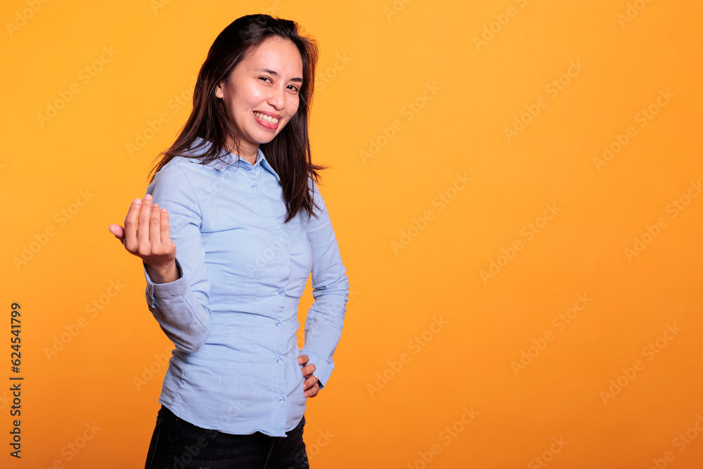 Filipino model inviting you to come here with a friendly smile on her confident expression, posing in studio over yellow background. Positive brunette woman is calling out with a finger gesture Filipino model inviting you to come here with a friendly smile on her confident expression, posing in studio over yellow background. Positive brunette woman is calling out with a finger gesture