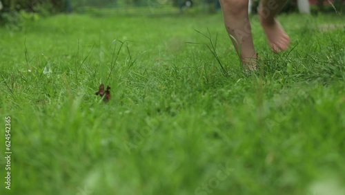 A little girl with bare feet on the grass. Sandals in the summer, hot summer and rest. Green grass, for children, lawn near the house. The little one likes to walk barefoot on the grass.