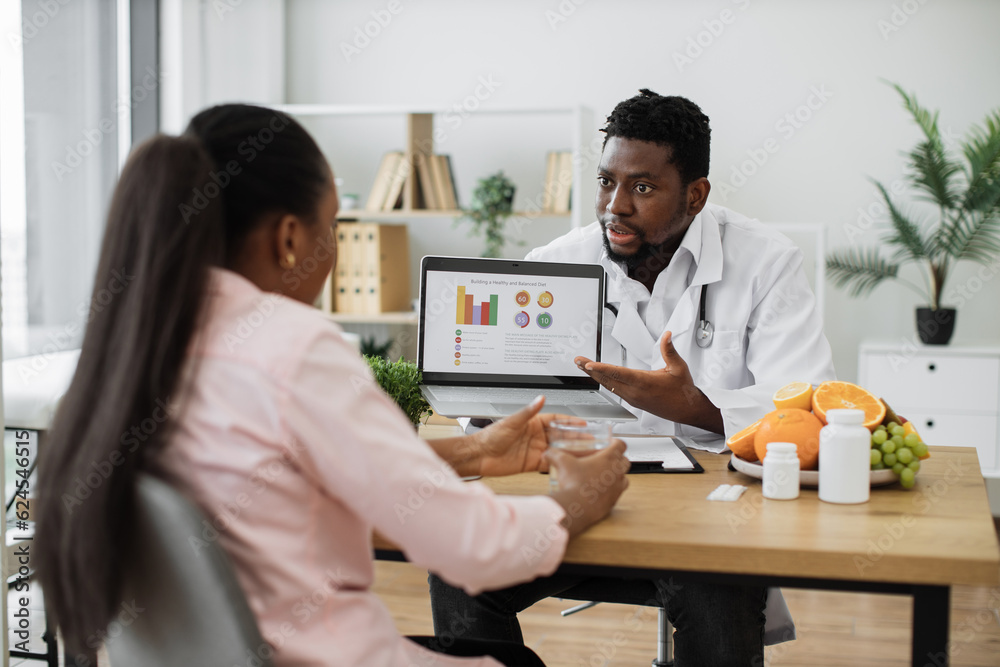 Female patient with long ponytail visiting doctor in private polyclinic. Experienced food expert in white medical uniform and stethoscope analyzing treatment effectiveness using graphs on laptop. Female patient with long ponytail visiting doctor in private polyclinic. Experienced food expert in white medical uniform and stethoscope analyzing treatment effectiveness using graphs on laptop.