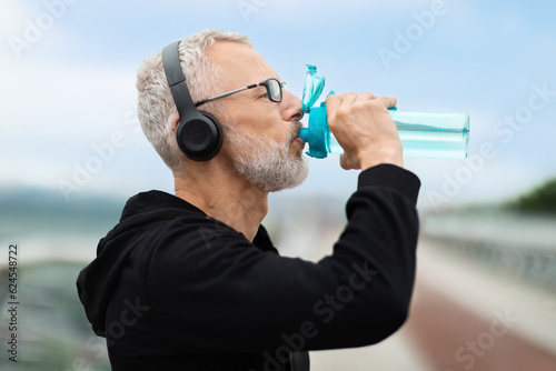 Closeup of elderly sportsman drinking water, running outdoor