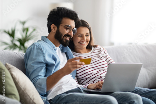 Happy indian couple with bank card and laptop at home
