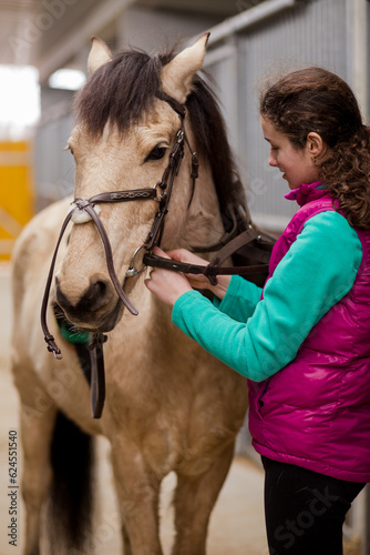 Horse riding school. Young Hispanic female care and prepare horseback ride sport. In stable