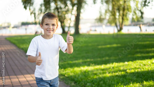 A joyful boy in a white T-shirt walks in a city park, near the embankment.
