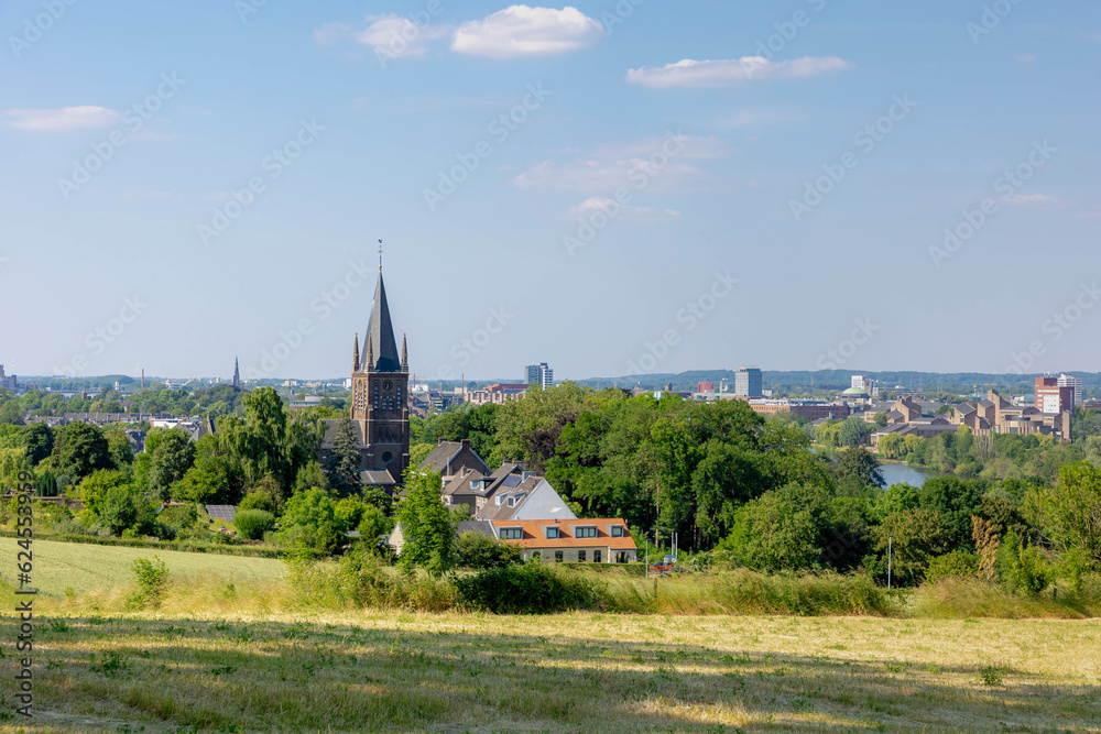 Fototapeta premium Summer landscape, The terrain of hilly countryside green grass meadow and farmland in Zuid-Limburg, Houses and church on hillside under blue sky, Maastricht is a capital city of Limburg, Netherlands.