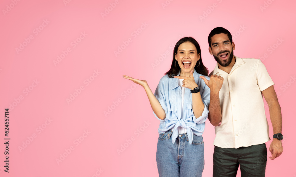Cute loving multiracial couple pointing at free space on pink Cute loving multiracial couple pointing at free space on pink