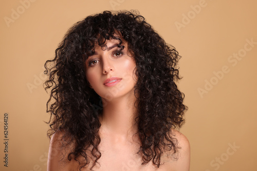 Beautiful young woman with long curly hair on beige background