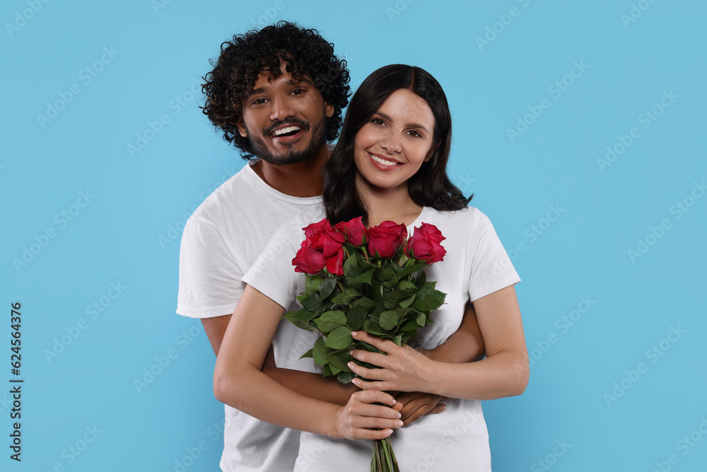 International dating. Happy couple with bouquet of roses on light blue background International dating. Happy couple with bouquet of roses on light blue background