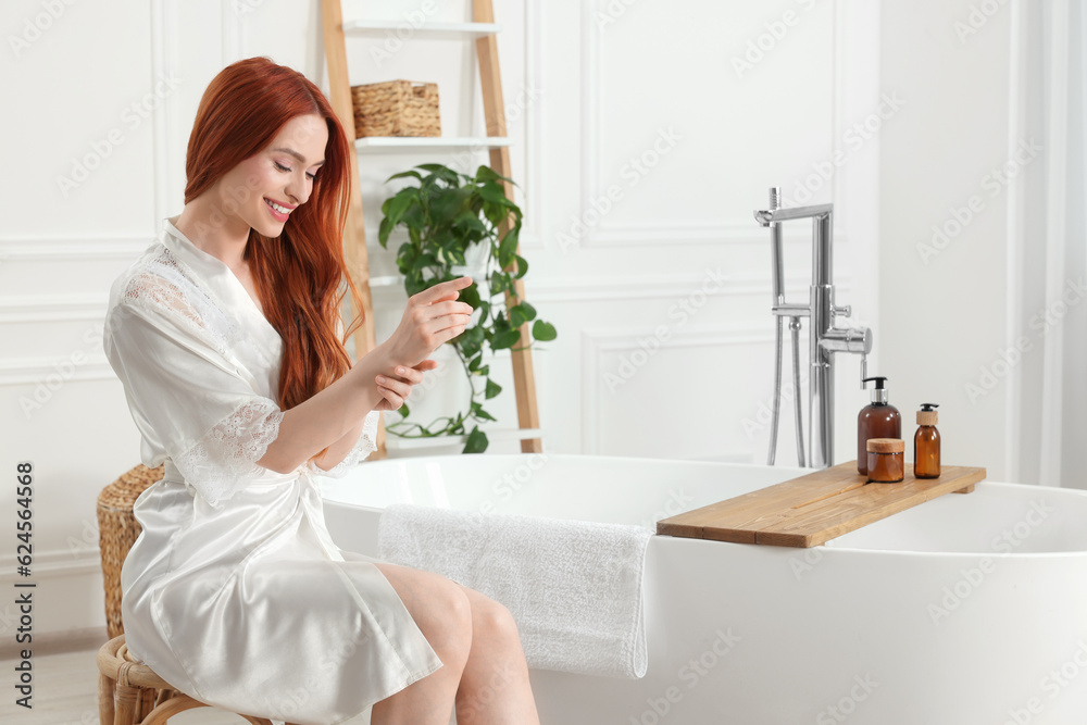 Beautiful young woman touching her smooth arms in bathroom, space for text Beautiful young woman touching her smooth arms in bathroom, space for text
