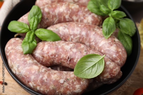 Raw homemade sausages and basil leaves in bowl on table, closeup