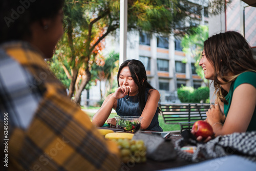 Laughing student girls having a snack at the college campus while they are resting from studying
