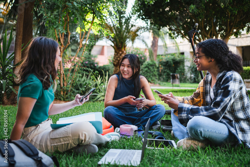 Three smiling university students sitting on the grass while they are resting of classes.