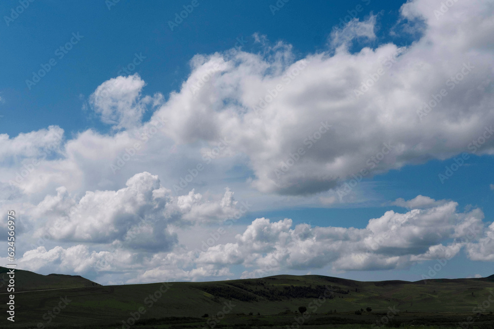 Photo of the steppe in summer, with beautiful clouds in the blue sky, the endless steppe at the foot of high hills under a warm summer sky. Khakassia, Siberia, Russia.