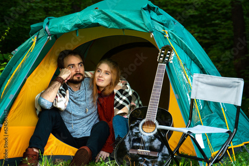 Pensive young couple sitting in camping tent hugging together