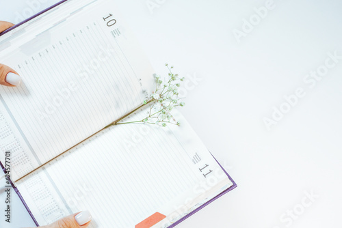 Opened diary with green small flowers between pages lying on white table. Woman holding sketchpad with empty notes. photo