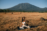 Portrait of a young, beautiful girl, of European appearance, in a white yoga suit, posing, stretching, doing yoga, against the backdrop of a mountain in a field with dry grass.
