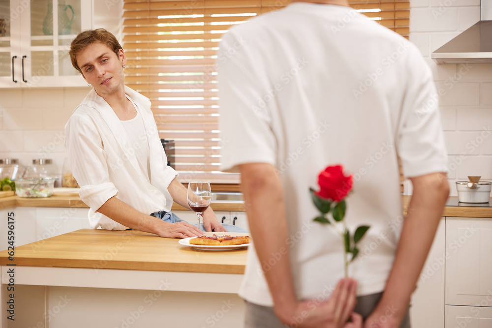 young gay couple looking at boyfriend and holding rose behind his back for surprise in the kitchen young gay couple looking at boyfriend and holding rose behind his back for surprise in the kitchen