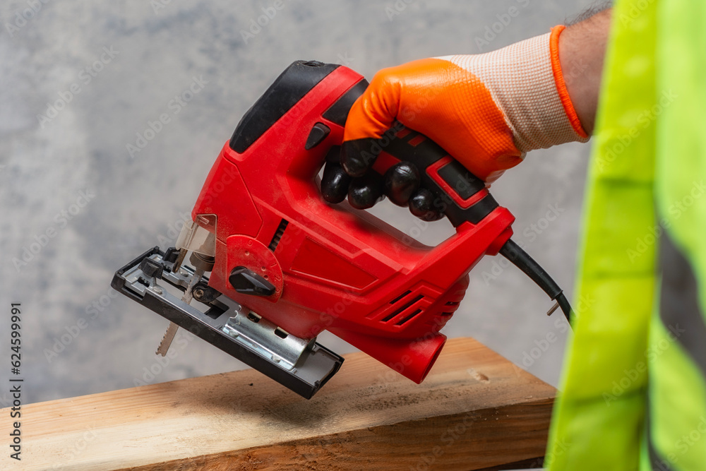 Male worker holds a close-up jigsaw electric in his hands against the background of a concrete wall.