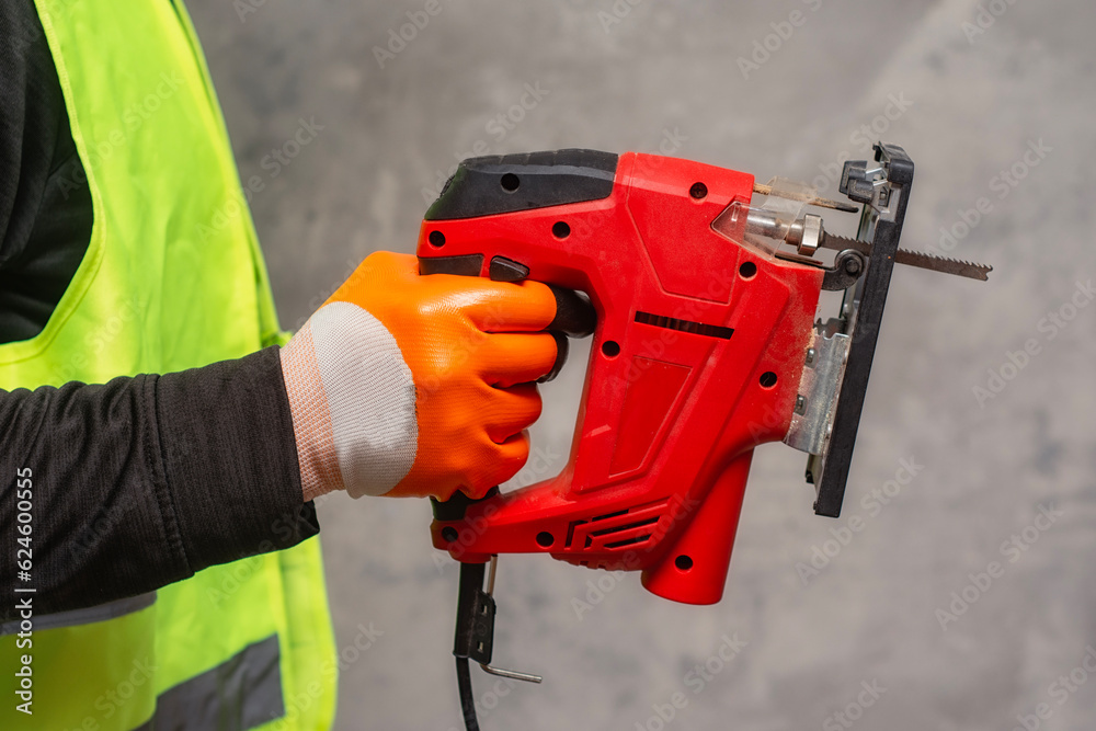 Male worker holds a close-up jigsaw electric in his hands against the background of a concrete wall. Male worker holds a close-up jigsaw electric in his hands against the background of a concrete wall.