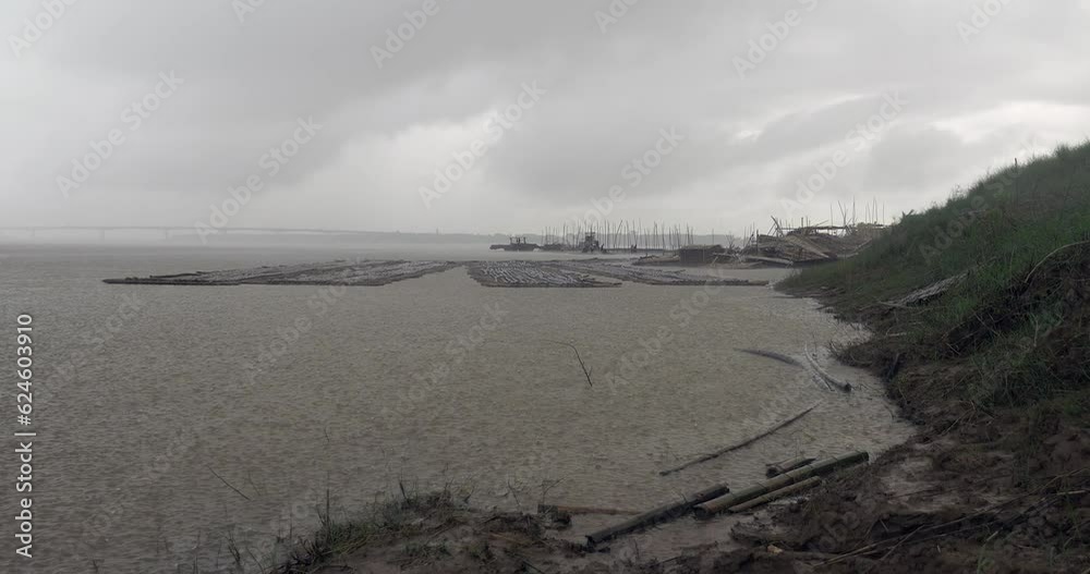 Heavy rain along the river bank. Workers cutting and moving bamboo poles stored in the background Heavy rain along the river bank. Workers cutting and moving bamboo poles stored in the background