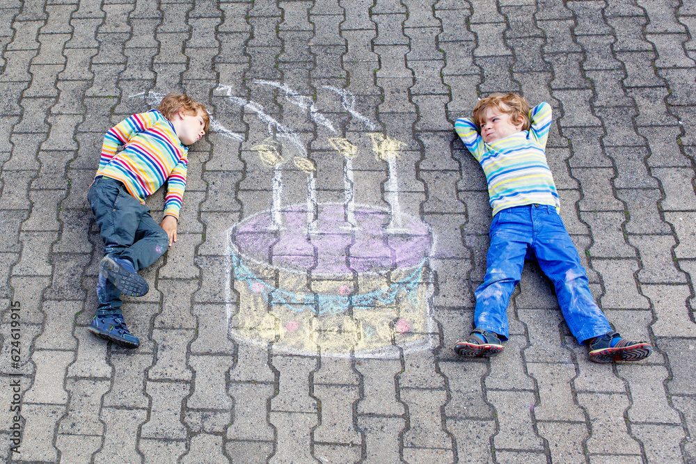 Two happy little kids having fun with big birthday cake picture drawing with colorful chalks. Creative leisure for children outdoors in summer. Kids blowing candles Two happy little kids having fun with big birthday cake picture drawing with colorful chalks. Creative leisure for children outdoors in summer. Kids blowing candles